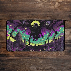 Puede incluir: Una alfombrilla de escritorio rectangular con una ilustración oscura y surrealista de una criatura de múltiples ojos que se cierne sobre una ciudad con un gran edificio con cúpula. La obra utiliza una paleta de colores vibrantes morado, verde neón y amarillo.