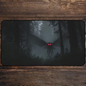 May include: A black rectangular mousepad featuring a dark, eerie forest scene. A large, winged creature with glowing red eyes hovers in the misty background. The design evokes a sense of mystery and the unknown.