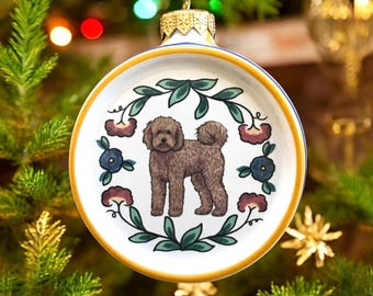 Könnte beinhalten: Runder, weißer Weihnachtsschmuck mit einer braunen Hundeillustration, umgeben von grünen Blättern und floralen Akzenten. Der Schmuck hat eine gold-blaue Umrandung und eine silberne Aufhängeschlaufe. Festliche Weihnachtsdekoration.