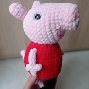 Może przedstawiać: Różowa dziana świnka z czerwoną koszulą i czarnymi butami. Świnka ma białe oko i różowy nos.