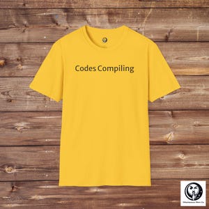 May include: A yellow t-shirt with the text "Codes Compiling" printed in black on the front.