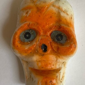 May include: A white and orange Halloween skull decoration with blue eyes. The skull is made of plastic and has a string attached to the top.