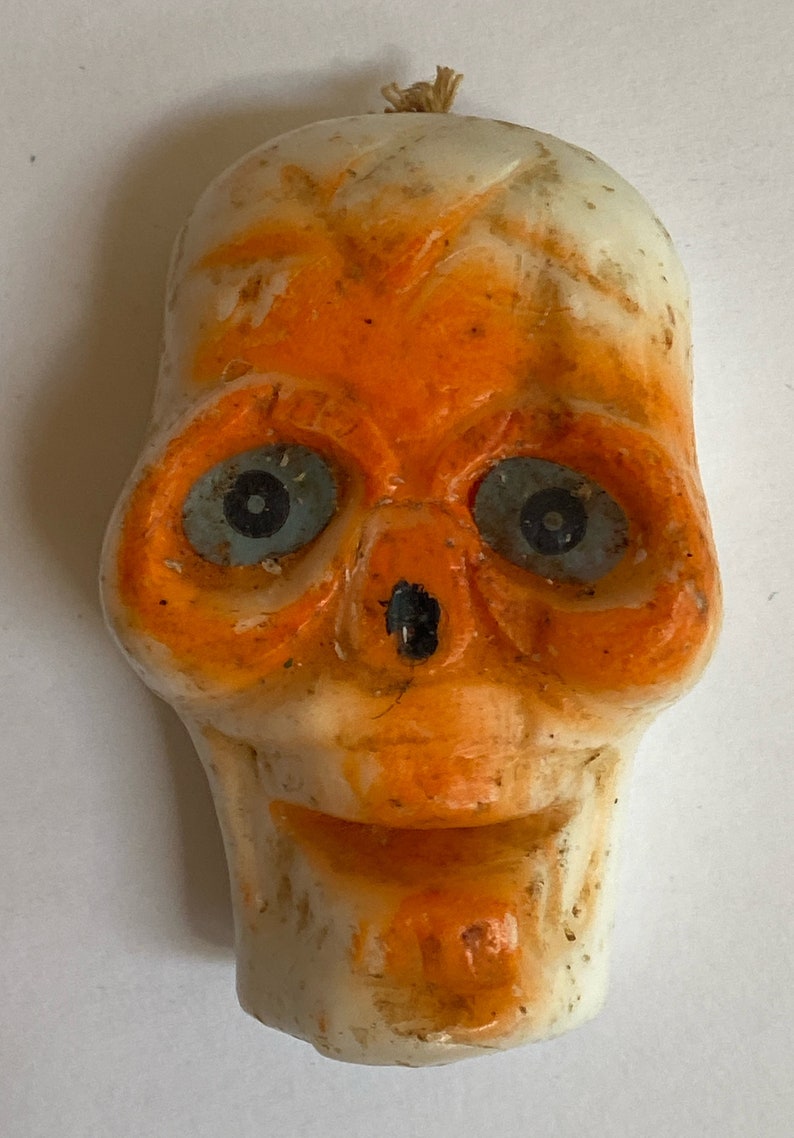 May include: A white and orange Halloween skull decoration with blue eyes. The skull is made of plastic and has a string attached to the top.