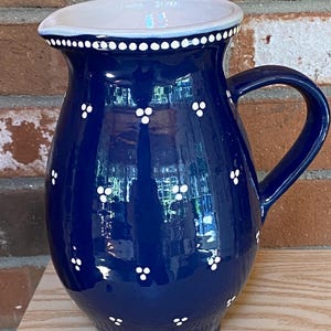 May include: A deep navy blue ceramic pitcher featuring a glossy finish and a hand-painted pattern of small white three-dot clusters arranged in rows. The pitcher has a wide spout, a curved handle, and a white interior rim with a dotted border.