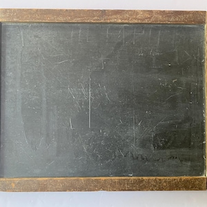 May include: A rectangular, vintage chalkboard with a dark gray surface and a weathered, brown wooden frame. The chalkboard shows signs of use with visible scratches and markings, suggesting it was used for writing or drawing.