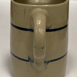 May include: A cream-colored ceramic pitcher with a blue stripe design. The pitcher has a wide mouth and a handle.
