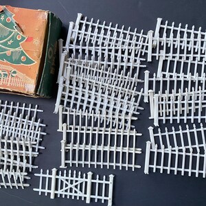 May include: A set of white plastic picket fence pieces for model building or miniature crafting. The pieces are designed to be assembled into a fence.