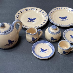 May include: A blue and white ceramic tea set with a bird design. The set includes a teapot, creamer, sugar bowl, teacup, and saucers. The saucers have the alphabet printed around the edge.