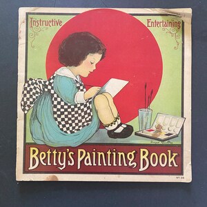May include: A vintage children's painting book with a red, white, and blue cover. The cover features a young girl sitting and drawing with a red sun behind her. The title of the book is "Betty's Painting Book" and the words "Instructive" and "Entertaining" are printed on the cover.