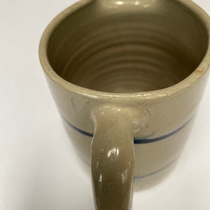May include: A cream-colored ceramic pitcher with a blue stripe around the middle and a handle. The pitcher has a wide mouth and a rounded bottom.
