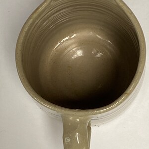 May include: A light gray ceramic pitcher with a handle. The pitcher has a smooth, glazed finish and a slightly rounded shape.
