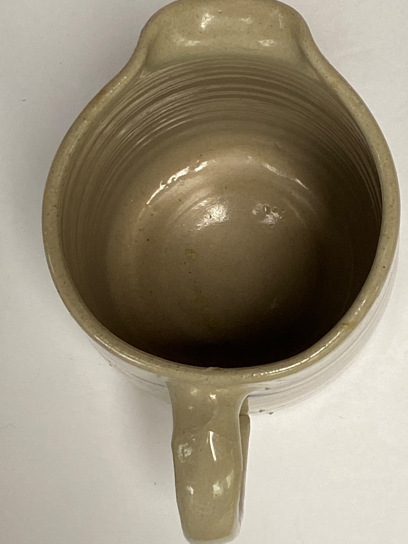 May include: A light gray ceramic pitcher with a handle. The pitcher has a smooth, glazed finish and a slightly rounded shape.