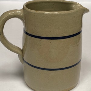 May include: A beige stoneware pitcher with two blue bands around the body. The pitcher has a rounded body and a handle.