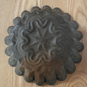 May include: A dark gray metal mold with a fluted edge and a decorative, raised, star-shaped design in the center.