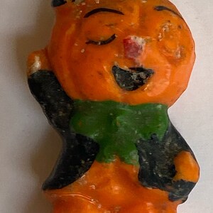 May include: A vintage Halloween candle shaped like a pumpkin with a black hat, green scarf, and a smiling face.