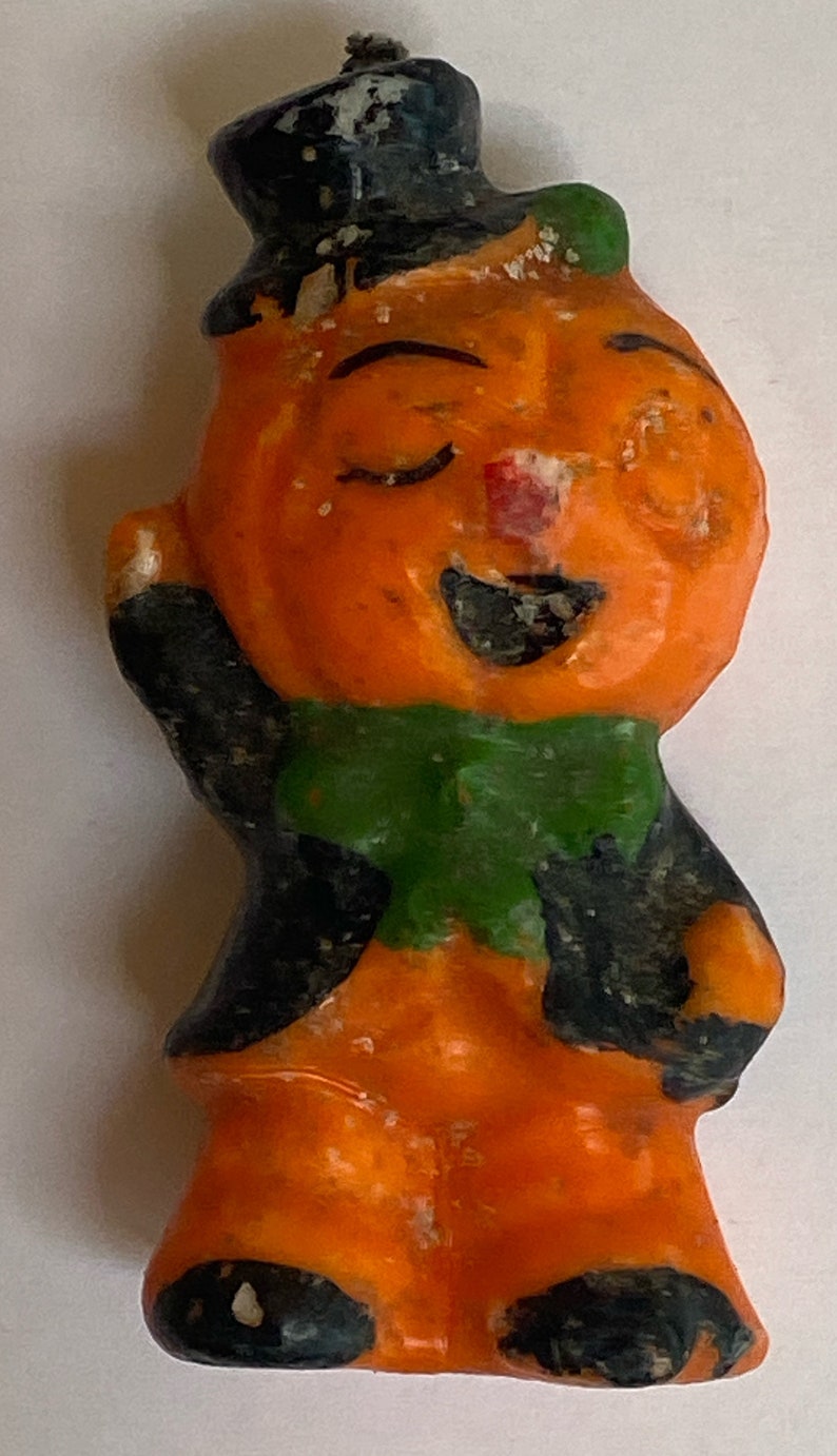 May include: A vintage Halloween candle shaped like a pumpkin with a black hat, green scarf, and a smiling face.