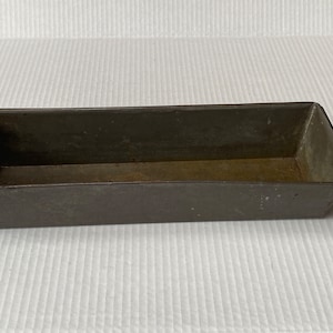 May include: A vintage metal loaf pan with a rectangular shape and a dark gray color. The pan has a slightly worn surface and is ideal for baking bread or other baked goods.