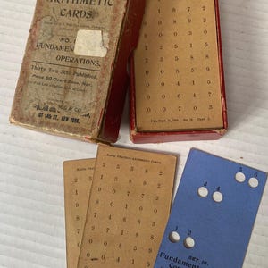 May include: An antique arithmetic card set with a red box and several cards. The box reads "Rapid Practice Arithmetic Cards" and "Fundamental Operations." The cards feature rows of numbers and a blue card with perforations for concrete work.