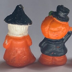 May include: Four Halloween-themed candle figurines. A white ghost, a witch with a black hat and orange dress, a pumpkin with a black hat and orange face, and a white ghost with a red hat and orange trousers.