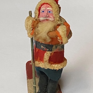 May include: A vintage Santa Claus figurine, dressed in a red coat with white trim, blue pants, and black boots. He wears a red hat and has a white beard. The figure is holding a wooden staff and standing on a wooden sled.