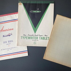 May include: Three vintage paper products: a white typewriter tablet with green and black design, a white air mail tablet with red and blue stripes, and a blank gridded paper sheet.