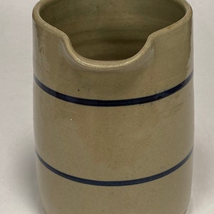 May include: A tan stoneware pitcher with two blue bands around the body. The pitcher has a wide mouth and a rounded base.