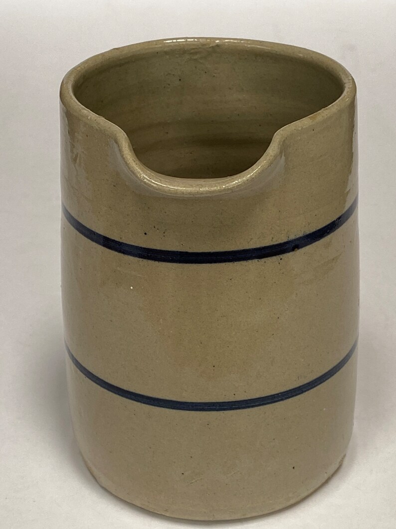 May include: A tan stoneware pitcher with two blue bands around the body. The pitcher has a wide mouth and a rounded base.