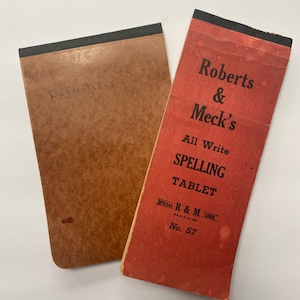 May include: Two vintage spelling tablets. The red tablet has the text "Roberts & Meck's All Write SPELLING TABLET SPECIAL R & M LINES No. 57". The brown tablet has the text "Definitions" written on it.