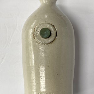 May include: A white stoneware bottle with a green stopper. The bottle has a circular mark with the text "D.C.H. POTTERY WKS BOSTON, MASS."