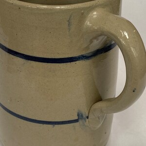 May include: A stoneware pitcher with a blue glaze and two blue stripes around the body. The pitcher has a handle and a wide mouth.