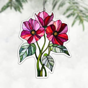 May include: A stained glass floral ornament featuring three flowers in shades of red, pink, and purple with yellow centers. The flowers are connected by green stems and leaves. The ornament hangs from a silver chain.