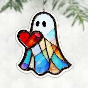 May include: A stained-glass style ghost ornament holding a red heart. The ghost has a white body with black eyes and a colourful, geometric design in shades of blue, yellow, and orange. It hangs from a silver chain.