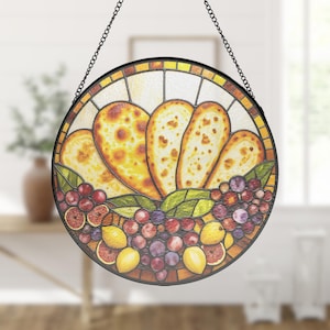 May include: A round stained glass window with a black metal frame and hanging chain. The design features a cluster of fruit, including grapes, lemons, and oranges, with a central arrangement of bread-like shapes.