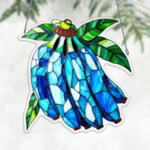 May include: Stained glass banana bunch in shades of blue, white, and green. The banana bunch is hanging from a chain. The leaves are green with white and dark green accents. The bananas are a mosaic of blue and white glass.