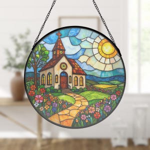May include: A stained glass window hanging with a black chain. The window depicts a small church with a red roof, a green lawn, a stone path, and a bright yellow sun in a blue sky.