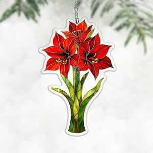 Op de afbeelding: Een decoratieve hanger met een levendige illustratie van rode amaryllisbloemen met groene stelen en bladeren. Het bloemmotief staat tegen een witte achtergrond, met een zilveren ketting om op te hangen. De hanger is ongeveer 10 cm hoog.