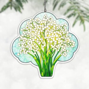 May include: A decorative hanging ornament featuring a stained glass style illustration of white baby's breath flowers with green stems against a light blue background. The ornament has a scalloped edge and a silver chain for hanging display.