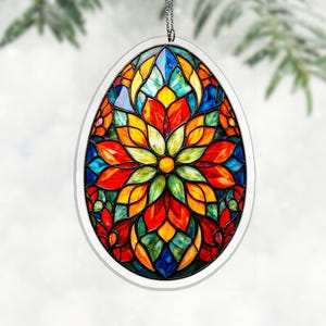 Op de afbeelding: Een ovaal glas-in-lood ornament met een bloemmotief. Het ornament heeft een witte rand en een ketting om op te hangen. Het bloemontwerp bestaat uit rode, oranje, gele, groene en blauwe glasstukken, wat een levendige en kleurrijke weergave creëert.