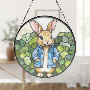 Può includere: Vetrata rotonda raffigurante un coniglio dei cartoni animati con una giacca blu. Il coniglio ha la pelliccia marrone e le orecchie rosa, su uno sfondo di fogliame verde. La finestra è incorniciata in nero e sospesa da una catena.