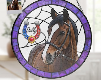 Pode incluir: Uma janela de vitral pendurada com uma borda roxa e uma imagem de cabeça de cavalo no centro. O cavalo é castanho com uma estrela branca na testa e uma rédea preta. O nome "Dolly" está escrito em vermelho e azul em uma ferradura.