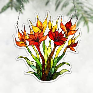 May include: A stained glass floral panel featuring vibrant red, orange, and yellow flowers with green leaves. The artwork is outlined in white and hangs from a silver chain. The design resembles a stylized bouquet.
