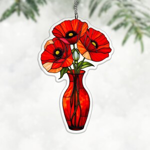 May include: A decorative ornament featuring a vibrant red vase holding three bright red poppies with black centers and green leaves. The ornament is suspended by a silver chain, perfect for adding a touch of floral elegance to any space.