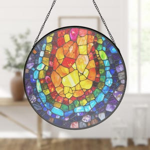 May include: A circular stained glass window with a colourful mosaic pattern. The window displays a range of hues, including red, orange, yellow, green, blue, and purple. It is framed in black and suspended by a chain.