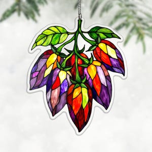 May include: A colorful stained-glass style ornament featuring a cluster of stylized flowers and leaves. The flowers are a mix of red, orange, yellow, and purple, with green stems and leaves. The ornament hangs from a silver chain.