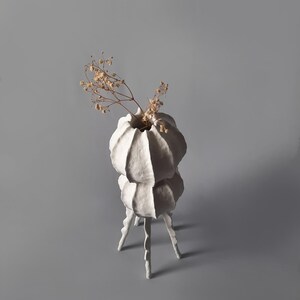 May include: White ceramic vase with a unique, organic shape and three legs. The vase is filled with dried flowers.