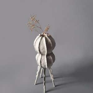 May include: White ceramic vase with a textured, organic shape. The vase has two bulbous sections and three legs. Dried flowers are in the vase.