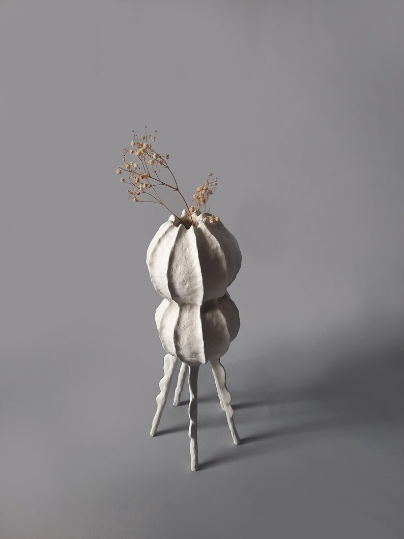 May include: White ceramic vase with a textured, organic shape. The vase has two bulbous sections and three legs. Dried flowers are in the vase.