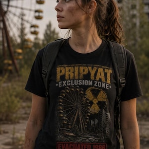 Könnte beinhalten: Ein schwarzes T-Shirt mit einem Grafikdruck, der den Text PRIPYAT EXCLUSION ZONE, ein Riesenrad, ein Strahlensymbol und den Text EVACUATED 1986 zeigt. Das Shirt enthält die Koordinaten 51.4081 N, 30.0571 E in einer abgenutzten gelb-roten Schrift.