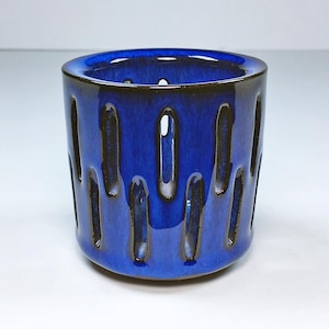 May include: A cobalt blue ceramic planter with a decorative cut-out design. The planter has a dark brown glaze on the rim and inside.