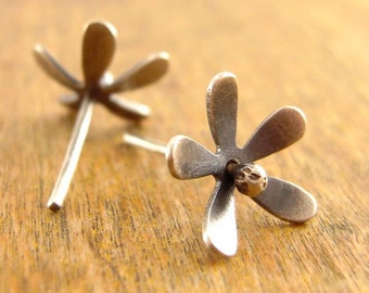 May include: A pair of silver-toned flower stud earrings. Each earring features five rounded petals and a small, round center. The earrings are displayed on a wooden surface, showcasing their delicate design and metallic finish.